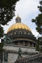 Saint Isaac`s Cathedral golden cupola dome, statues, granite columns behind green trees foliage on blue cloudy sky background