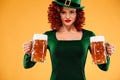 Saint Patricks Day. Young ginger Oktoberfest leprechaun, wearing green dress and hat, serving big beer mugs on orange Royalty Free Stock Photo