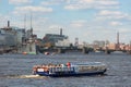 Small excursion ship with tourists sails on the Neva River opposite the legendary cruiser Aurora