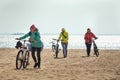 Three girls in bright jackets with bicycles are walking on a sandy beach Royalty Free Stock Photo