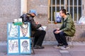 Street caricature portrait artist with a tourist getting his portrait drawn near Palace Square in Saint Petersburg, Russia