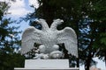 White doubleheaded metal eagle standing on the Park gate, against the background of trees and