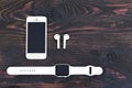 White smartphone iPhone 5S+, smartwatch Apple watch sport with a band and wireless headphones Airpods on the background