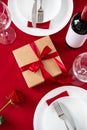 Saint Valentine`s Day table setting with cutlery, gift box, wine bottle, glasses, red roses on red background Royalty Free Stock Photo