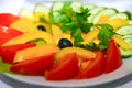 Salad of assorted vegetables in a plate stands on a festive table. Red tomatoes, cucumbers, olives, yellow pepper, parsley