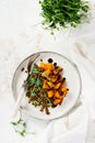 Salad with baked pumpkin, lentils and balsamic dressing garnished with peas microgreens on a light background.