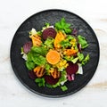 Salad: beetroot, pumpkin, corn and lettuce in a black plate on a white wooden background. Top view.