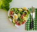 Salad cucumber tomato egg plate heart on a white wooden background