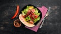 Salad of fresh vegetables and sausages in a black plate. On a wooden background. Royalty Free Stock Photo