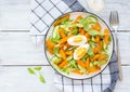 Salad of fried sweet potato or pumpkin, arugula, fresh cucumber and boiled egg on a white plate on a light wooden background. Royalty Free Stock Photo