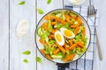 Salad of fried sweet potato or pumpkin, arugula, fresh cucumber and boiled egg on a white plate on a light wooden background. Royalty Free Stock Photo