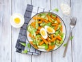 Salad of fried sweet potato or pumpkin, arugula, fresh cucumber and boiled egg on a white plate on a light wooden background. Royalty Free Stock Photo