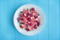 Salad of fruits and berries. Light heart-shaped watermelon salad, raspberries, blueberries in a white plate on a blue wooden Royalty Free Stock Photo