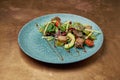 Salad with grilled tuna, arugula, cherry tomatoes, avocado and cucumber in a blue ceramic plate on a copper, metal background. Royalty Free Stock Photo