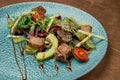 Salad with grilled tuna, arugula, cherry tomatoes, avocado and cucumber in a blue ceramic plate on a copper, metal background. Royalty Free Stock Photo