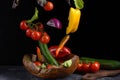 Salad ingredients levitation. Healthy vegetarian food is flying over a wooden bowl on a dark stone table with a cutting board and