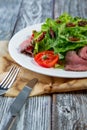 Salad leaves with sliced roast beef and sun-dried cherry tomatoes on wooden background Royalty Free Stock Photo