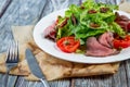 Salad leaves with sliced roast beef and sun-dried cherry tomatoes on wooden background Royalty Free Stock Photo