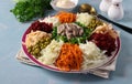 Salad with meat, peas, potatoes, carrots, beets, green onion and cabbage on a plate on blue background