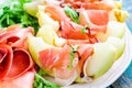 Salad of melon with thin slices of prosciutto, arugula leaves and balsamic sauce closeup