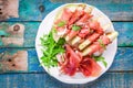 Salad of melon with thin slices of prosciutto, arugula leaves and balsamic sauce top view