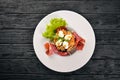 Salad with prosciutto, quail eggs, prunes and fresh vegetables on the plate. On a wooden background. Top view. Royalty Free Stock Photo