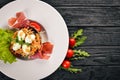 Salad with prosciutto, quail eggs, prunes and fresh vegetables on the plate. On a wooden background. Top view. Royalty Free Stock Photo