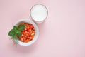 Salad of red tomatoes and orange bell peppers with a bunch of mint and dill with glass of milk on pink background with copy space.