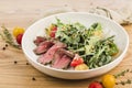 Salad with roast beef, arugula and cherry tomatoes in a plate on a light wooden background Royalty Free Stock Photo