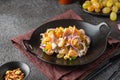 Salad of salted herring, tangerines, grapes and walnuts on a black plate on a dark concrete background. Herring dishes