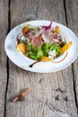 Salad with slices of bacon, persimmon and pieces of gorgonzola is beautifully presented on a white plate