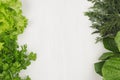 Salad, spinach, dill, parsley sheaves on white wood plank, top view, decorative border.