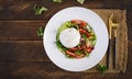 Salad with tomatoes and burrata cheese with lettuce and olive oil on wooden background. Royalty Free Stock Photo