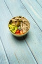 A salad with various types of diced tomato, avocado and lots of canned tuna in a golden bowl on a blue plank table