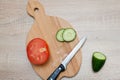 Salad vegetables, chopped cucumbers, a tomato and a kitchen knife lie on a wooden board Royalty Free Stock Photo