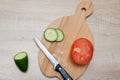 Salad vegetables, chopped cucumbers, a tomato and a kitchen knife lie on a wooden board Royalty Free Stock Photo