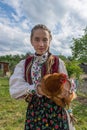 Salaj, Transylvania, Romania-May 14, 2020: Beautiful young girl in traditional Romanian folk costume holding a chicken at a