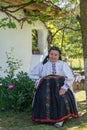 Salaj, Transylvania, Romania-May 14, 2018: old woman in traditional Romanian folk costume sitting in the garden in front of her Royalty Free Stock Photo