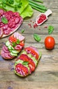 Salami sandwich with tomatoes and cucumbers next sliced salami and tomato and Basil leaves with salad on wooden background Royalty Free Stock Photo