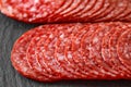 Salami sausage meat with bacon cut into circles in two rows close-up on slate stone plate, dark background, side view, selective