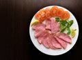Salami with sliced tomatoes, mint and lemon on a white plate.