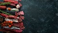 Salami and snacks. Sausage Fouet, sausages, salami, paperoni, on a black stone background. Top view. Royalty Free Stock Photo