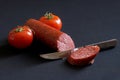 Salami, tomatoes and a sharp dangerous knife on a dark background. Concept and metaphor for male circumcision and male cosmetic