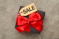 Sale price tag on black gift on grey concrete background. Black Friday sales discount composition