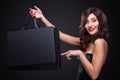 Sale. Young smiling woman showing shopping bag in black friday holiday. Girl on dark background with copy space Royalty Free Stock Photo