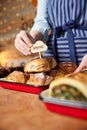 Sales Assistant In Bakery Putting Homemade Label Into Stack Of Freshly Baked Baked Cinnamon Buns Royalty Free Stock Photo