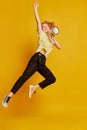 Full-length portrait of active young red-haired girl jumping with megaphone isolated on yellow studio background. Human Royalty Free Stock Photo