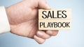 sales playbook on wooden block with in businessman hands