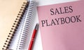 SALES PLAYBOOK word on the pink paper with office tools on white background