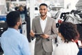 Salesman In Car Dealership Talking With Customers Helping Choose Auto